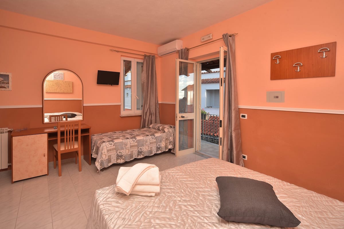 Ein Schlafzimmer mit Bett, Schreibtisch, Stuhl und kleinem Balkon.