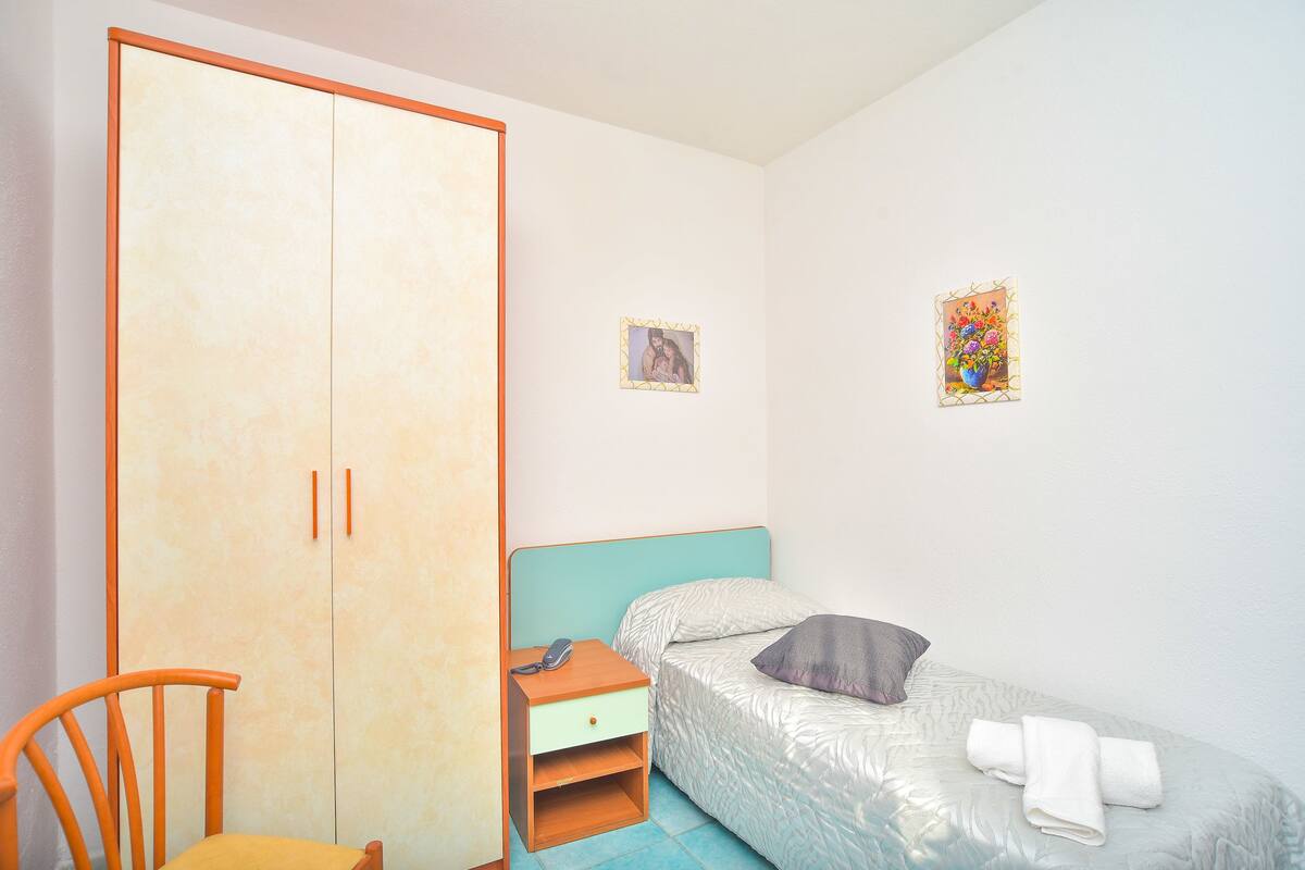 Ein Schlafzimmer mit einem Bett, einem Kleiderschrank, einem Stuhl und einem kleinen Nachttisch mit Telefon und Lampe.