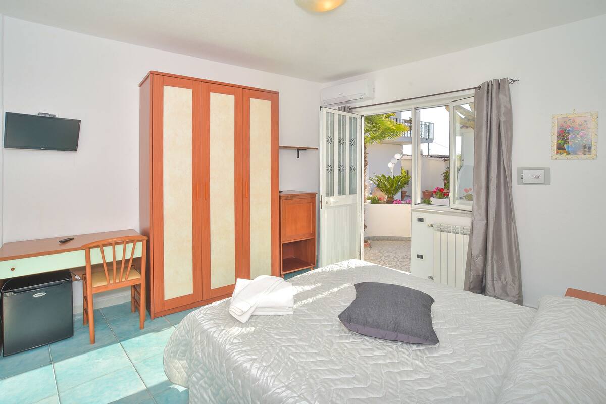 Ein Hotelzimmer mit Bett, Schreibtisch, Kleiderschrank, Fernseher und Blick auf den Balkon.