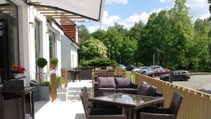An outdoor seating area with wicker furniture and a glass table, overlooking a parking area and greenery. - Hotel Golfi (Podebrady)