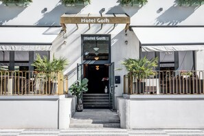 The entrance to Hotel Golfi with a clear sign, steps leading up to the entrance, and potted plants on either side.