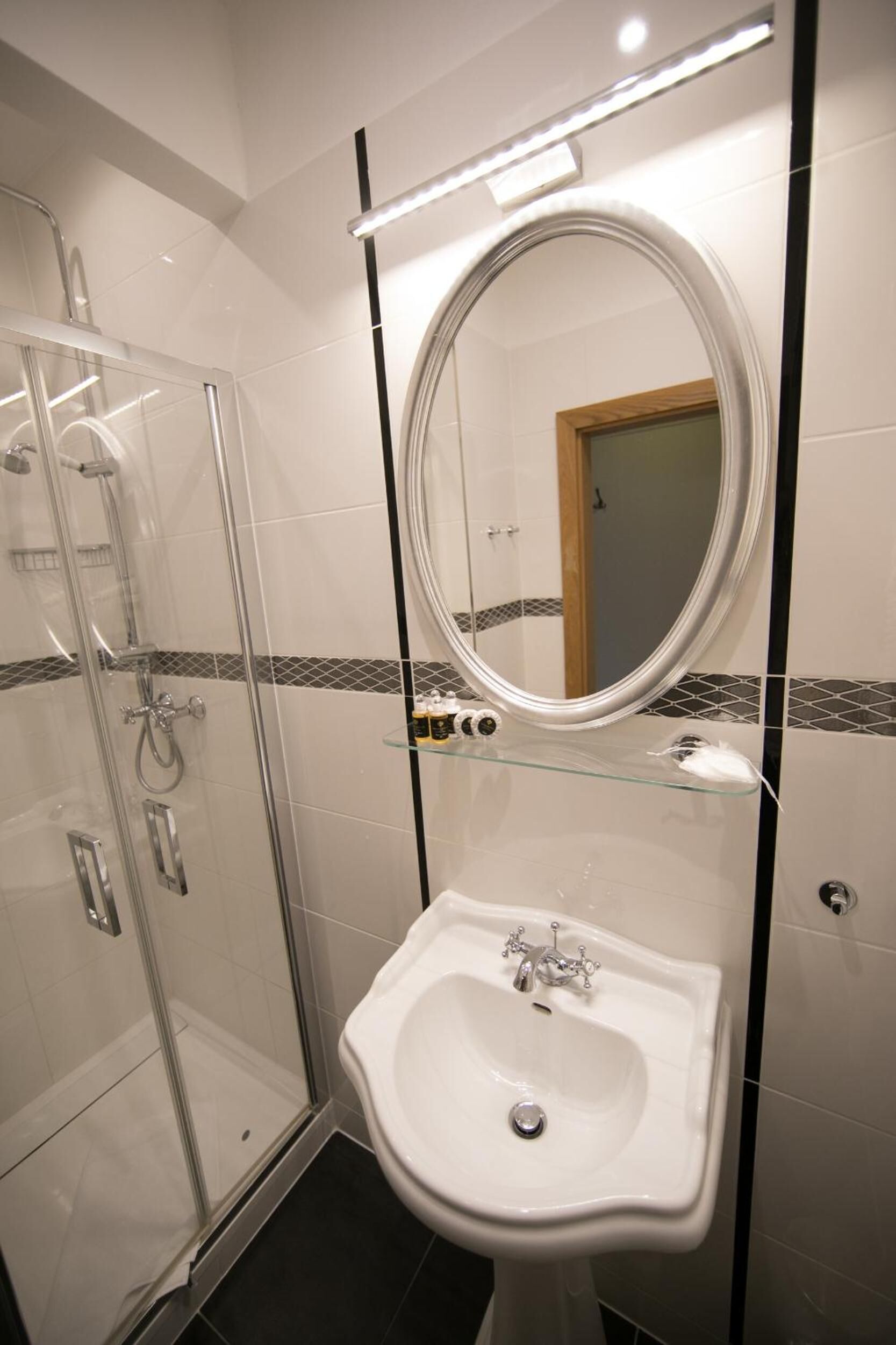 Un baño con cabina de ducha de vidrio, un lavamanos blanco y un espejo con una franja negra.