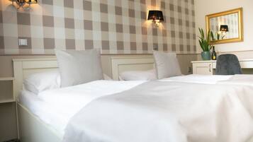 A hotel room with a large bed, two wall-mounted lamps, a mirror, and a desk with a chair.