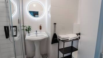 A modern bathroom with a glass shower enclosure, a pedestal sink, and a black shelf with towels.