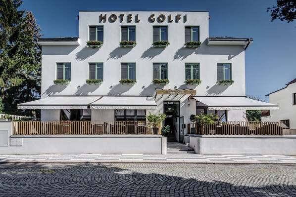 A modern hotel named "Hotel Golfi" with a white facade, multiple windows, and outdoor seating areas.