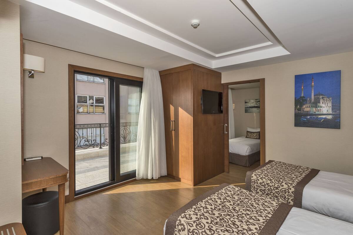 A hotel room with a bed, a desk, a chair, a TV, and a balcony with a view of a building.