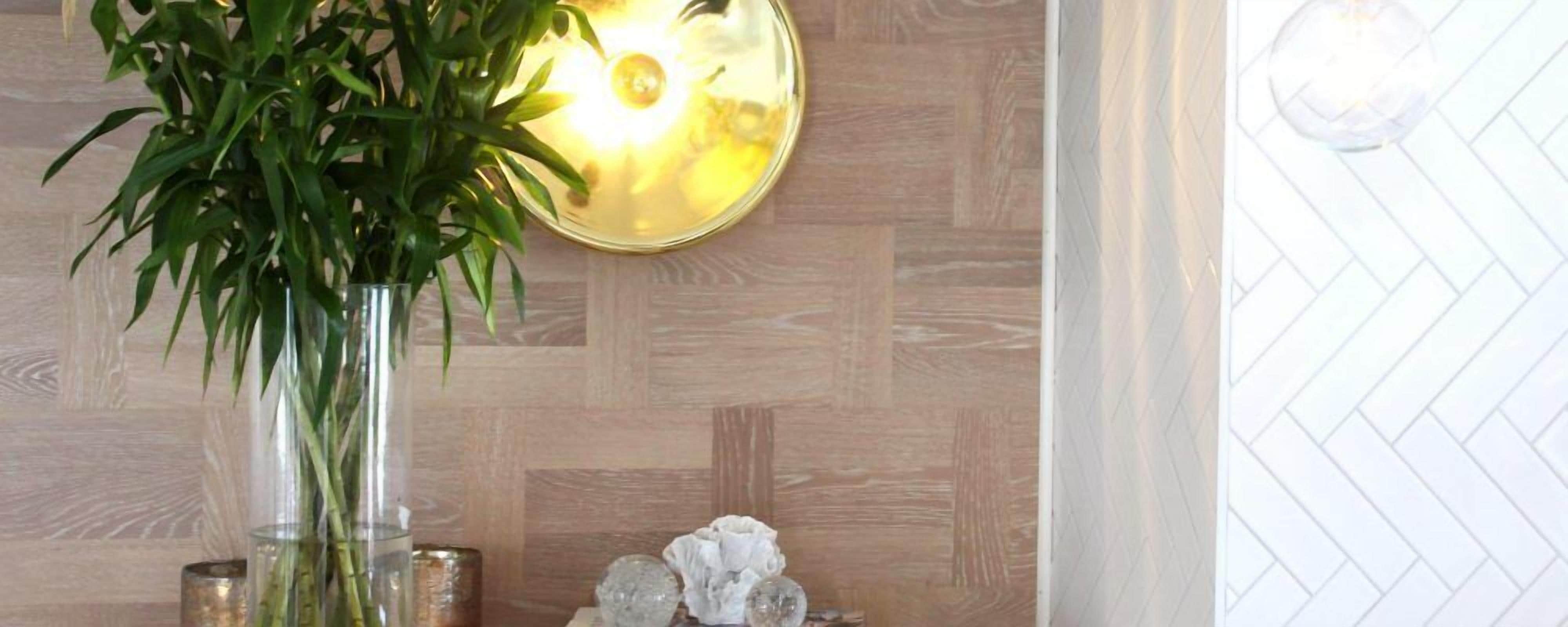 A room with a wooden wall, a potted plant, a decorative wall piece, and a textured white wall.