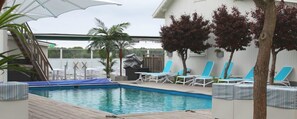 A pool area with a covered deck, lounge chairs, and a palm tree. - Strandhotellet (Öregrund)