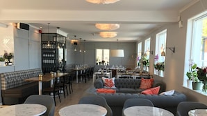 Ein modernes Restaurant mit verschiedenen Sitzgelegenheiten, darunter runde Tische, Sofas und eine Bar.