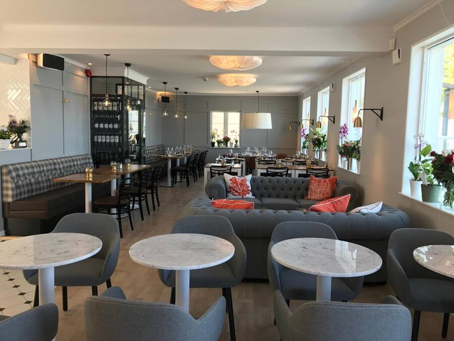 A modern restaurant with a mix of seating options including round tables, sofas, and a bar area.