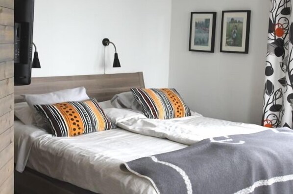 Una cama doble con almohadas estampadas, una lámpara de noche y dos cuadros en la pared.
