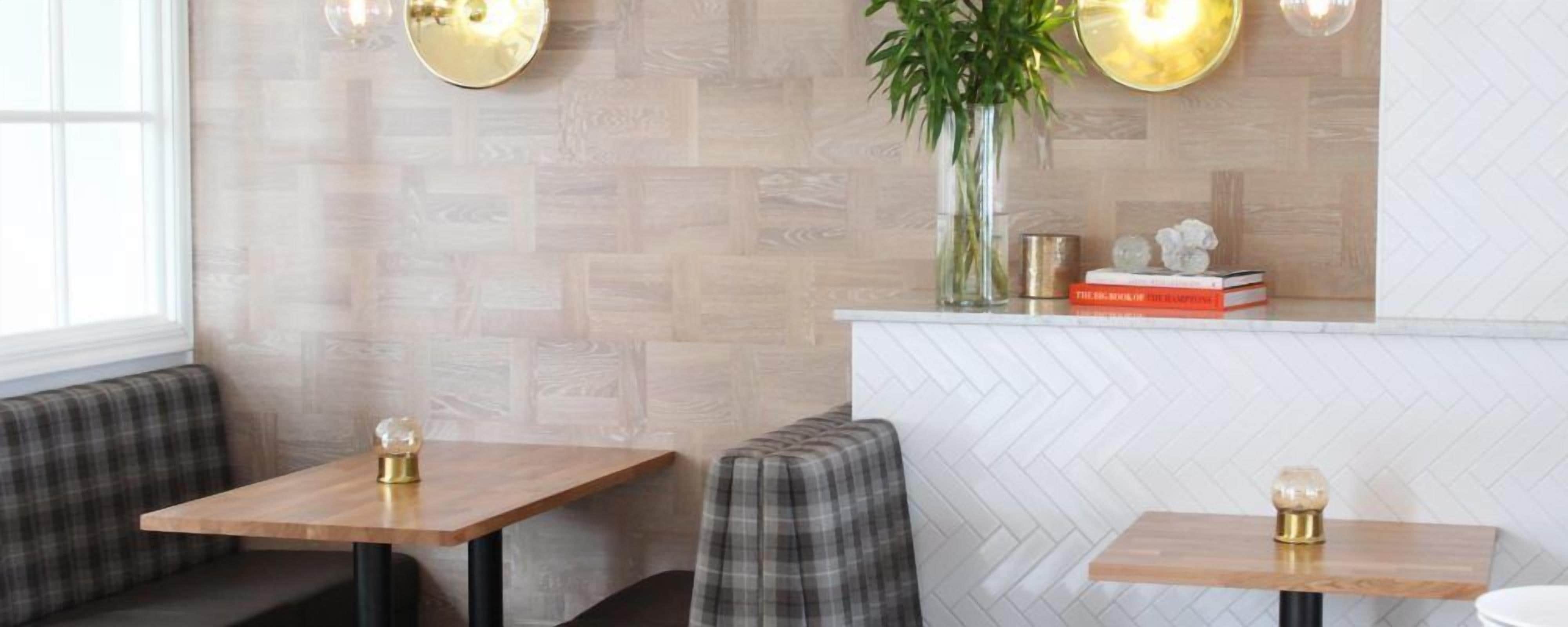 Un intérieur moderne avec deux tables en bois, un banc et un mur blanc orné d’un motif en chevrons.
