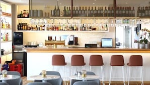 Eine Bar mit einer langen Theke, verschiedenen Sitzgelegenheiten wie Barhocker und runden Tischen sowie einer Auswahl an Flaschen und Gläsern in Regalen.