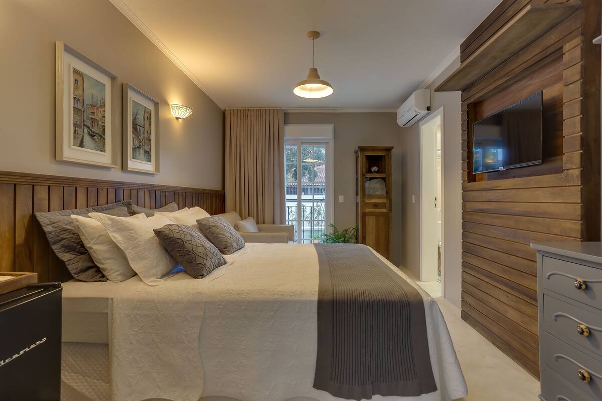 Une chambre à coucher avec un lit, un téléviseur fixé au mur en bois et des tableaux encadrés accrochés au mur.