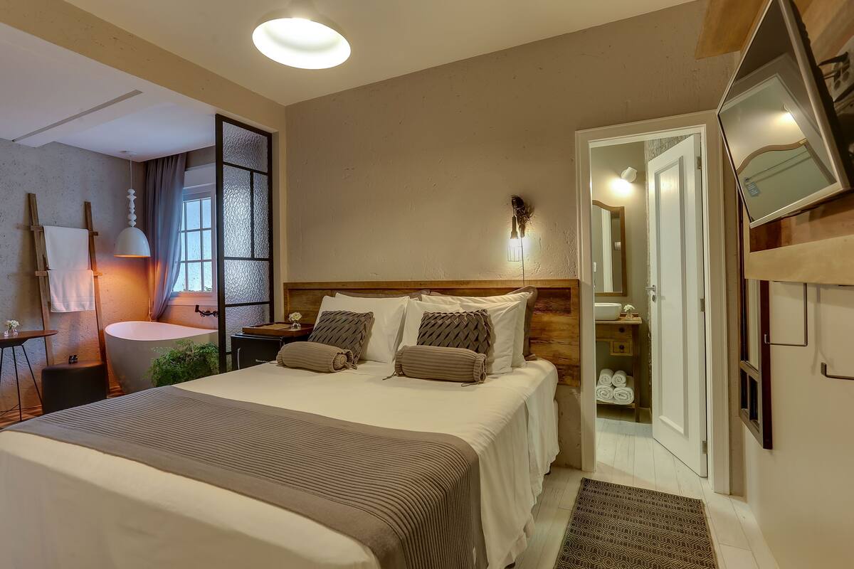 Une chambre d’hôtel avec un grand lit, des tables de chevet, un miroir, une petite table avec une lampe et une vue sur la salle de bain.