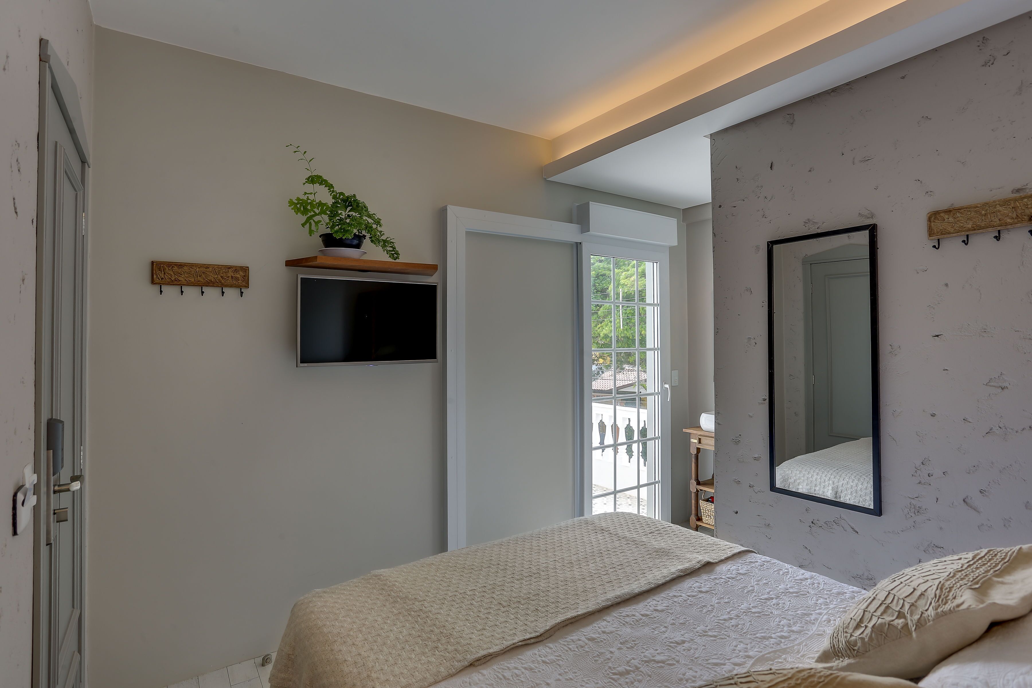 A bedroom with a bed, a mounted TV, a potted plant, and a large mirror on the wall.