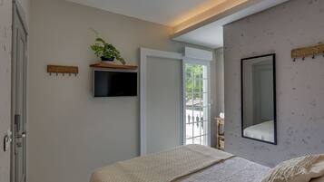 A bedroom with a bed, a mounted TV, a potted plant, and a large mirror on the wall.