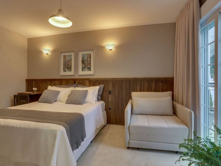 Ein Hotelzimmer mit einem großen Bett, einer Couch, zwei Wandlampen und einem mit Vorhängen drapierten Fenster.
