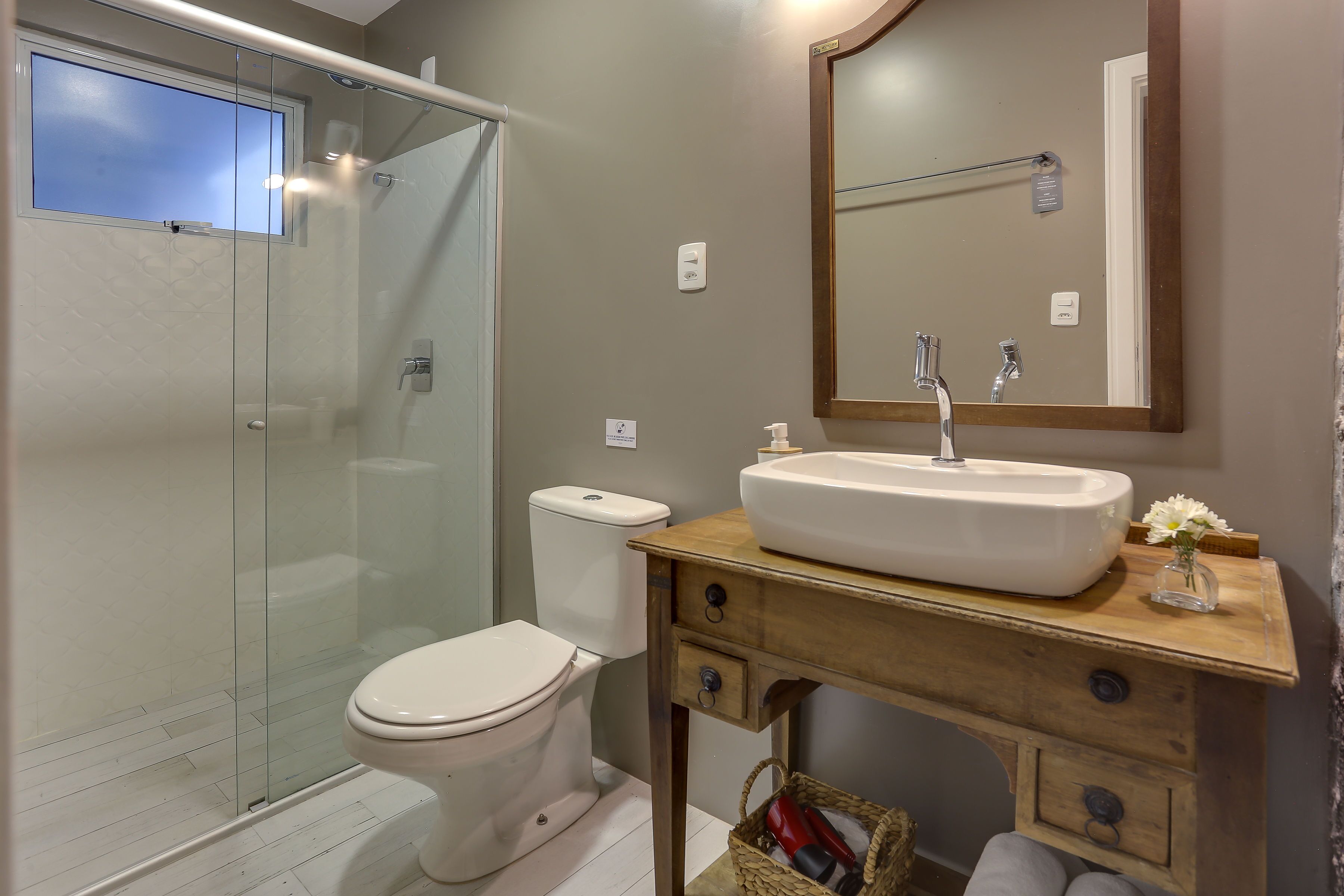 A bathroom with a glass shower enclosure, a white toilet, and a wooden vanity with a sink and mirror.