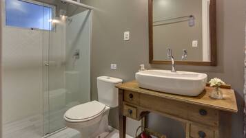 A bathroom with a glass shower enclosure, a white toilet, and a wooden vanity with a sink and mirror.