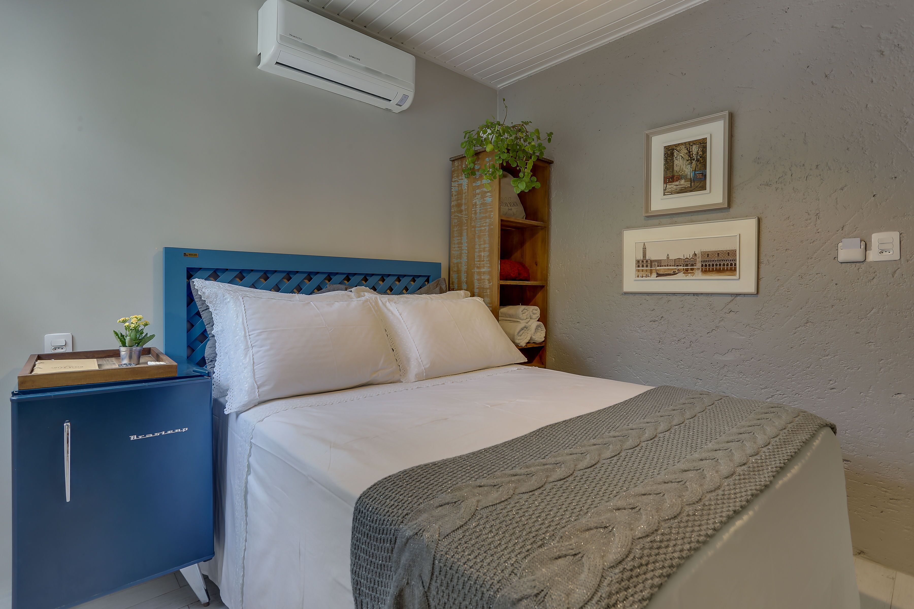 Un dormitorio con cama, un armario azul, aire acondicionado y cuadros en la pared.