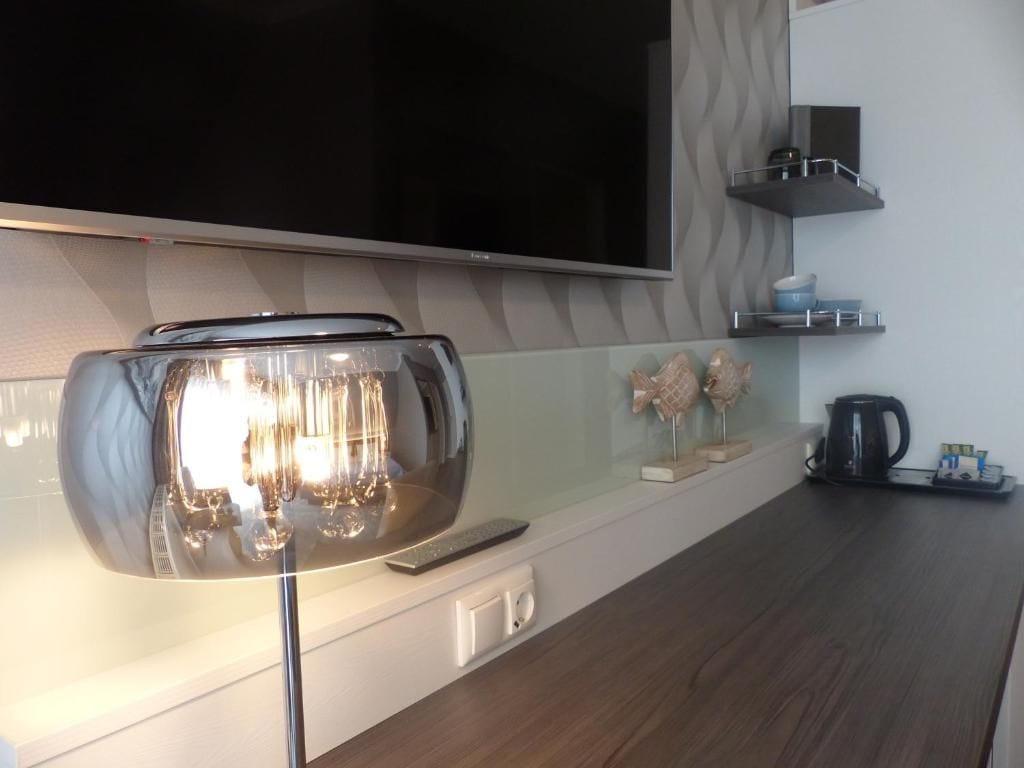 A modern kitchen with a flat-screen TV mounted above a countertop, a glass-top coffee table, and a kettle on the right.