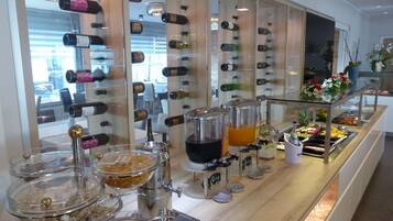 Una colazione a buffet con varie proposte di cibo e bevande, tra cui un distributore di succo e una scaffalatura per il vino.