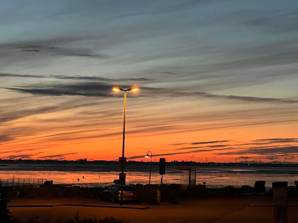 Ein Sonnenuntergang über einem Gewässer, im Vordergrund eine Straßenlaterne und ein Zaun.