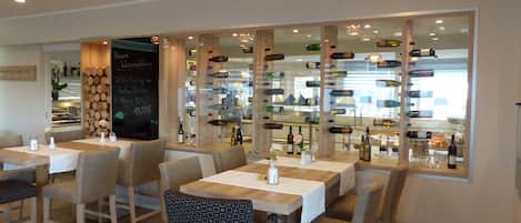 A restaurant with wooden tables and chairs, a wine display, and a chalkboard menu.