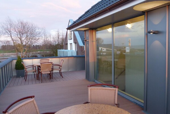 A modern outdoor deck with wicker furniture and a glass door leading to a covered area.