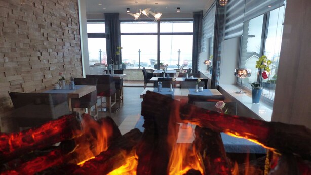 A modern dining area with a fireplace, large windows, and a view of the cityscape. - Strand Hotel Dangast (Varel)
