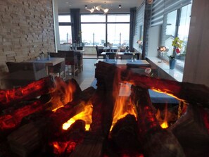 A modern dining area with a fireplace, large windows, and a view of the cityscape. - Strand Hotel Dangast (Varel)