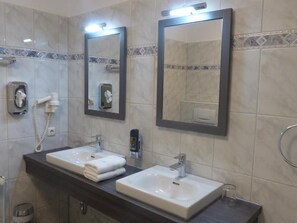 A bathroom with two sinks, a mirror, a towel dispenser, and a soap dispenser.