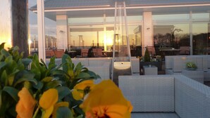 An outdoor seating area with modern furniture and a glass wall overlooking a building. - Strand Hotel Dangast (Varel)