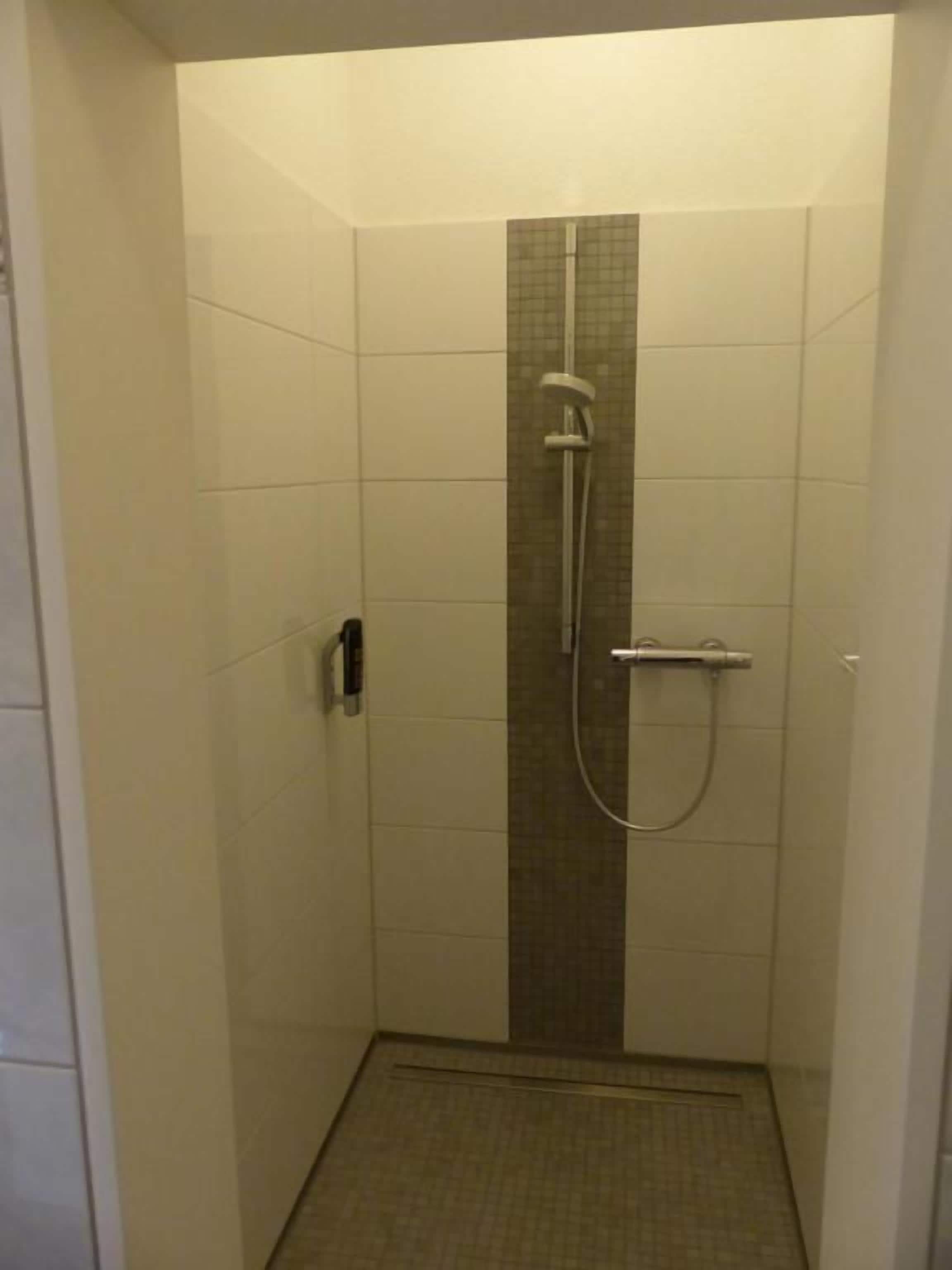Un box de ducha con pared de azulejos, un cabezal de ducha y un rociador de mano.