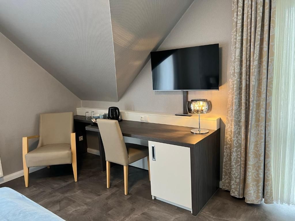 Ett modernt hotellrum med ett skrivbord, två stolar, en tv och ett litet kylskåp.