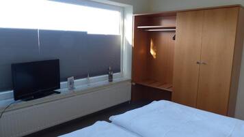 Ein Hotelzimmer mit einem Bett, einem Fernseher, einem Kleiderschrank und einem Fenster mit Jalousien.