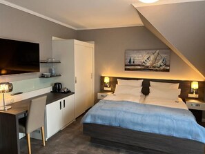 A bedroom with a bed, bedside tables, a desk, and a television. - Strand Hotel Dangast (Varel)