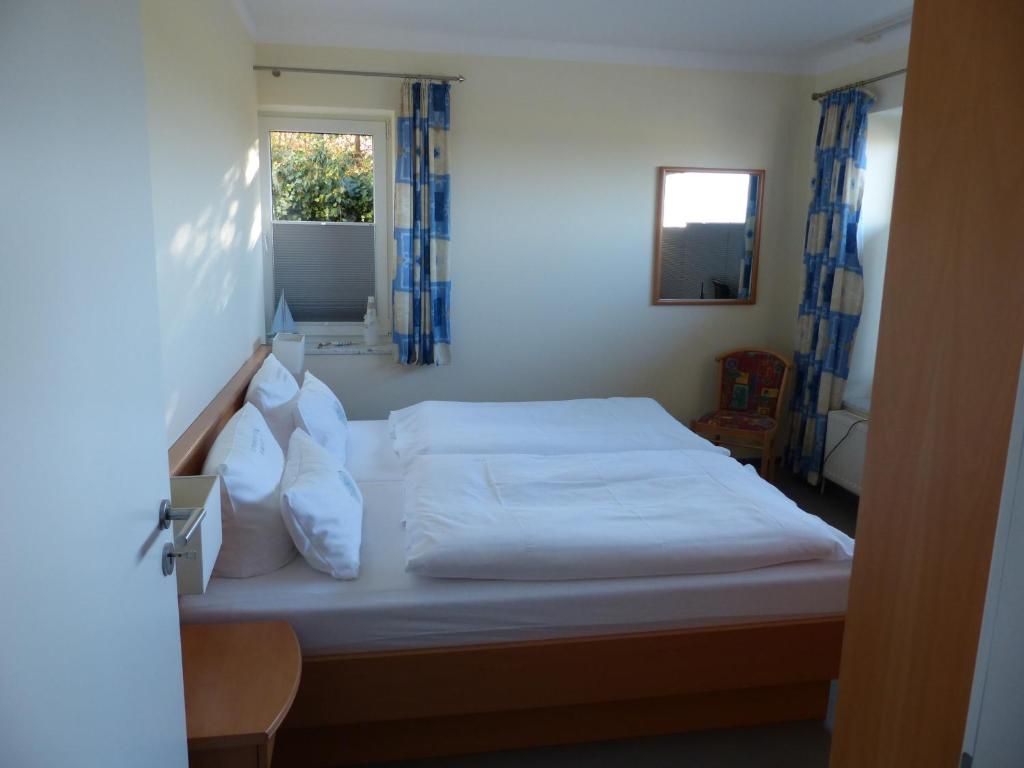 A bedroom with a bed, a window with curtains, a bedside table, and a mirror on the wall.