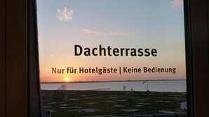 A view of a sunset over a water body with the text 'Dachterrasse Nur für Hotelgäste | Keine Unterkunft' indicating a terrace for hotel guests only. - Strand Hotel Dangast (Varel)
