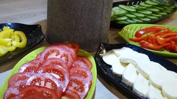 A table with various food items including sliced tomatoes, cucumbers, bell peppers, and cheese.