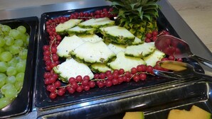 A buffet with various fruits including grapes, red currants, pineapple, and melon slices. - Pension an Bord (Varel)