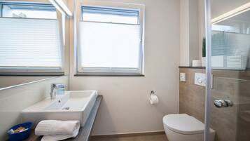 Un baño moderno con lavamanos blanco, inodoro y cabina de ducha de vidrio.