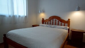 A bedroom with a wooden bed, two bedside lamps, a window with sheer curtains, and a tiled floor. - Cabanas Nagual (El Hoyo)