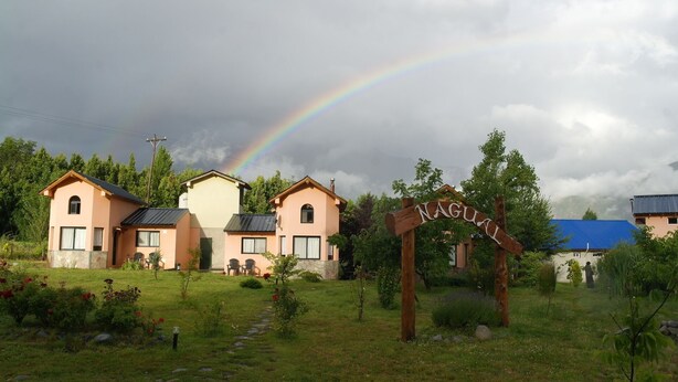 A residential area with a rainbow, houses, and a wooden sign with the word "NAGUIL". - Cabanas Nagual (El Hoyo)