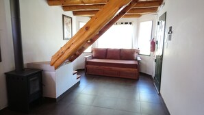 A cozy room with a wooden staircase, a sofa, and a wood-burning stove. - Cabanas Nagual (El Hoyo)