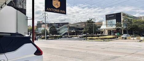 A sign for Antons Inn with a crown logo, a parking lot, and a modern building with a sign for All Day Supermarket in the background.