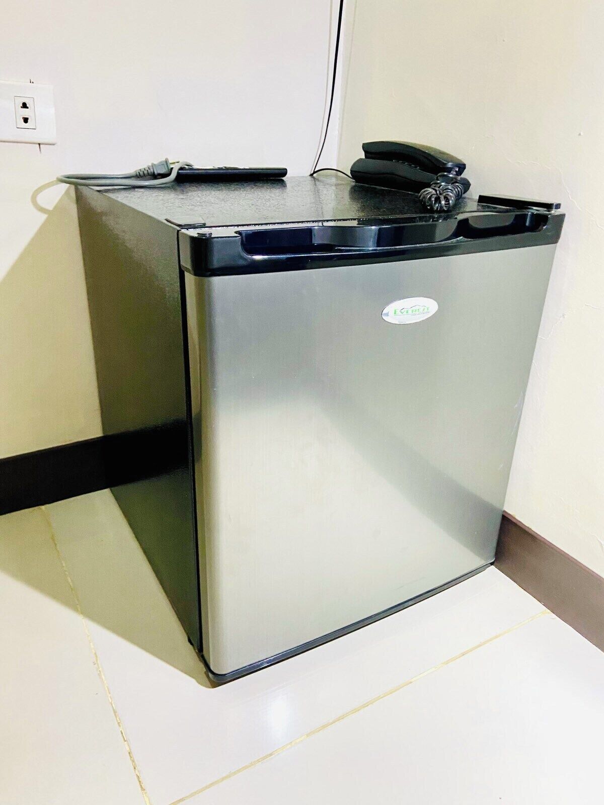 Un refrigerador compacto de acero inoxidable con parte superior negra y un pequeño logotipo en la parte frontal.