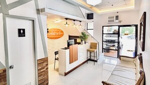 A reception area with a counter, a waiting area with a sofa, and a women's restroom sign. - Anton's Inn Hotel (Balanga)