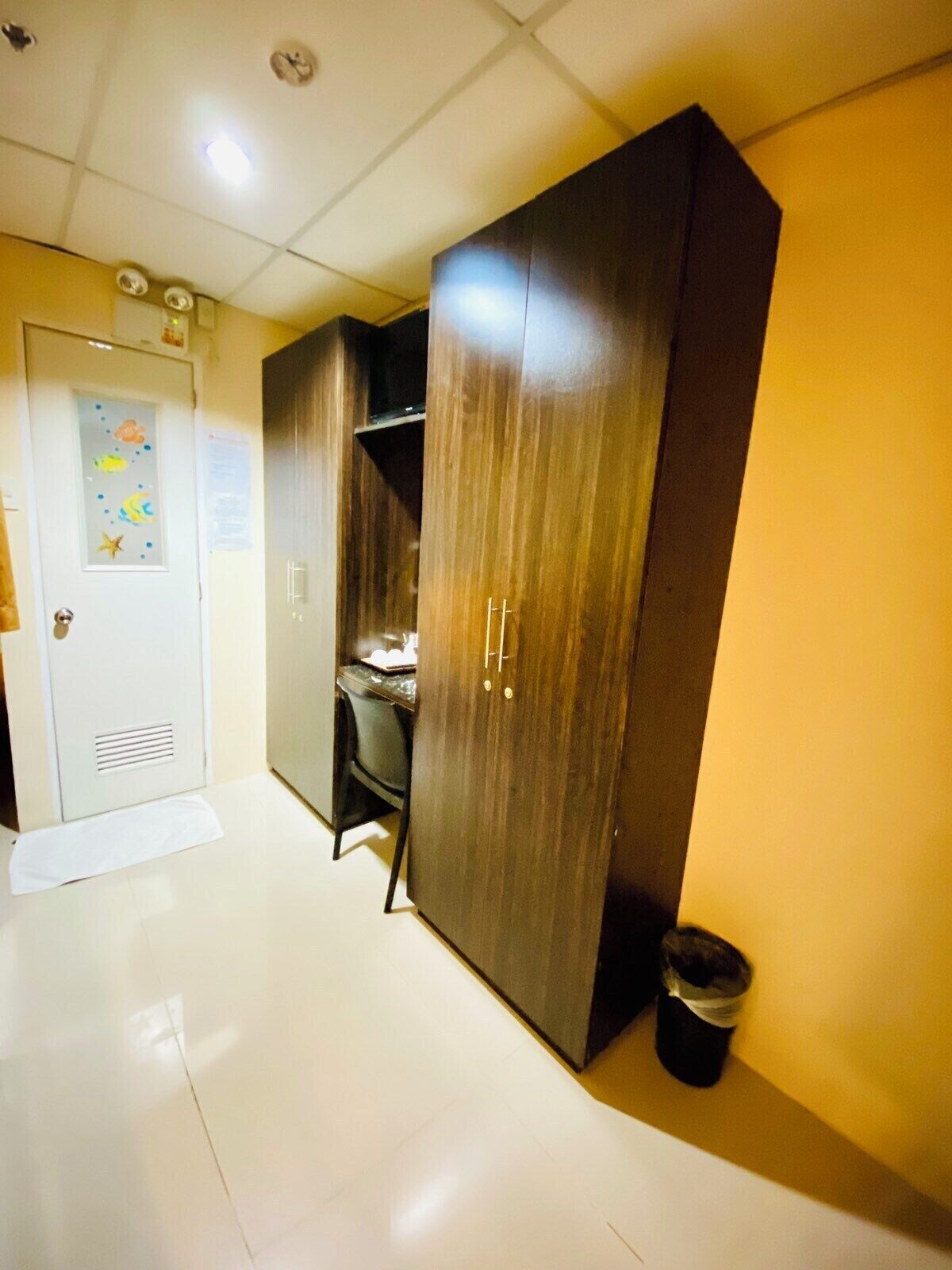 A hallway with a wooden wardrobe, a desk, and a trash bin.